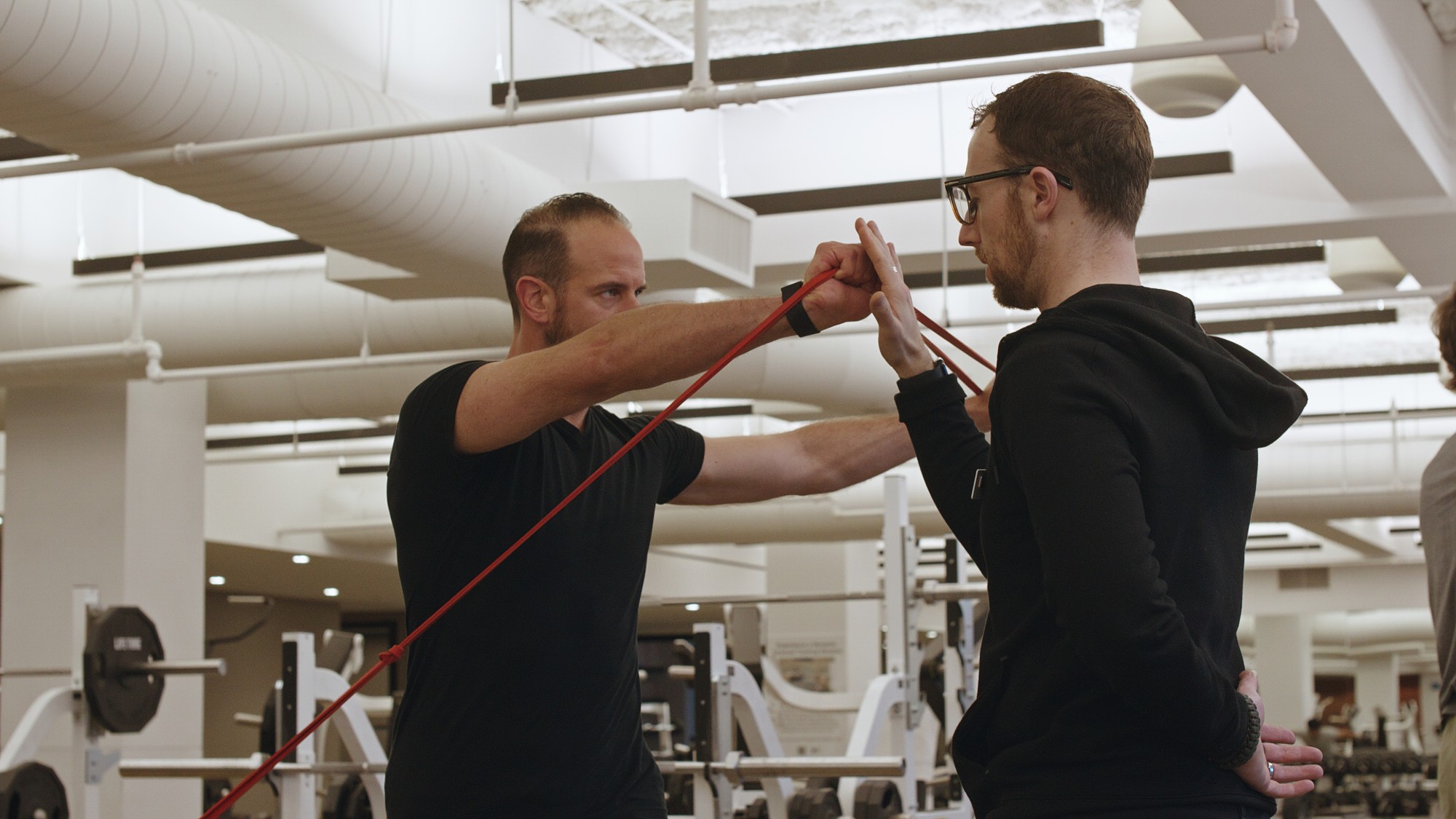 A Life Time master trainer coaching a client through resistance-band work on the gym floor